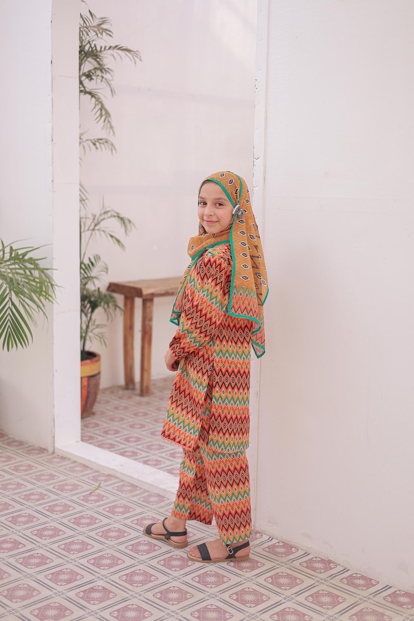 Woman in a colorful traditional outfit standing in a room with plants and a mirror.