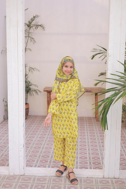 Woman in a yellow traditional outfit standing in a room with plants.