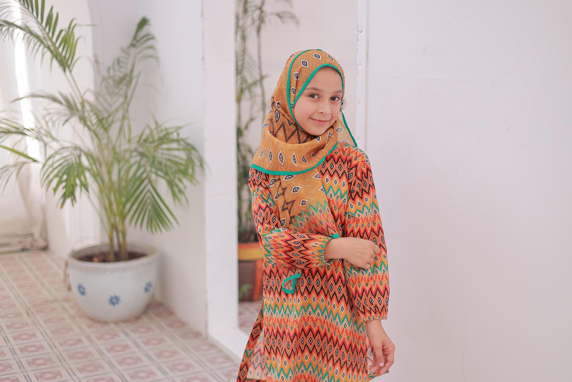 Woman wearing a colorful dress and headscarf indoors with plants in the background