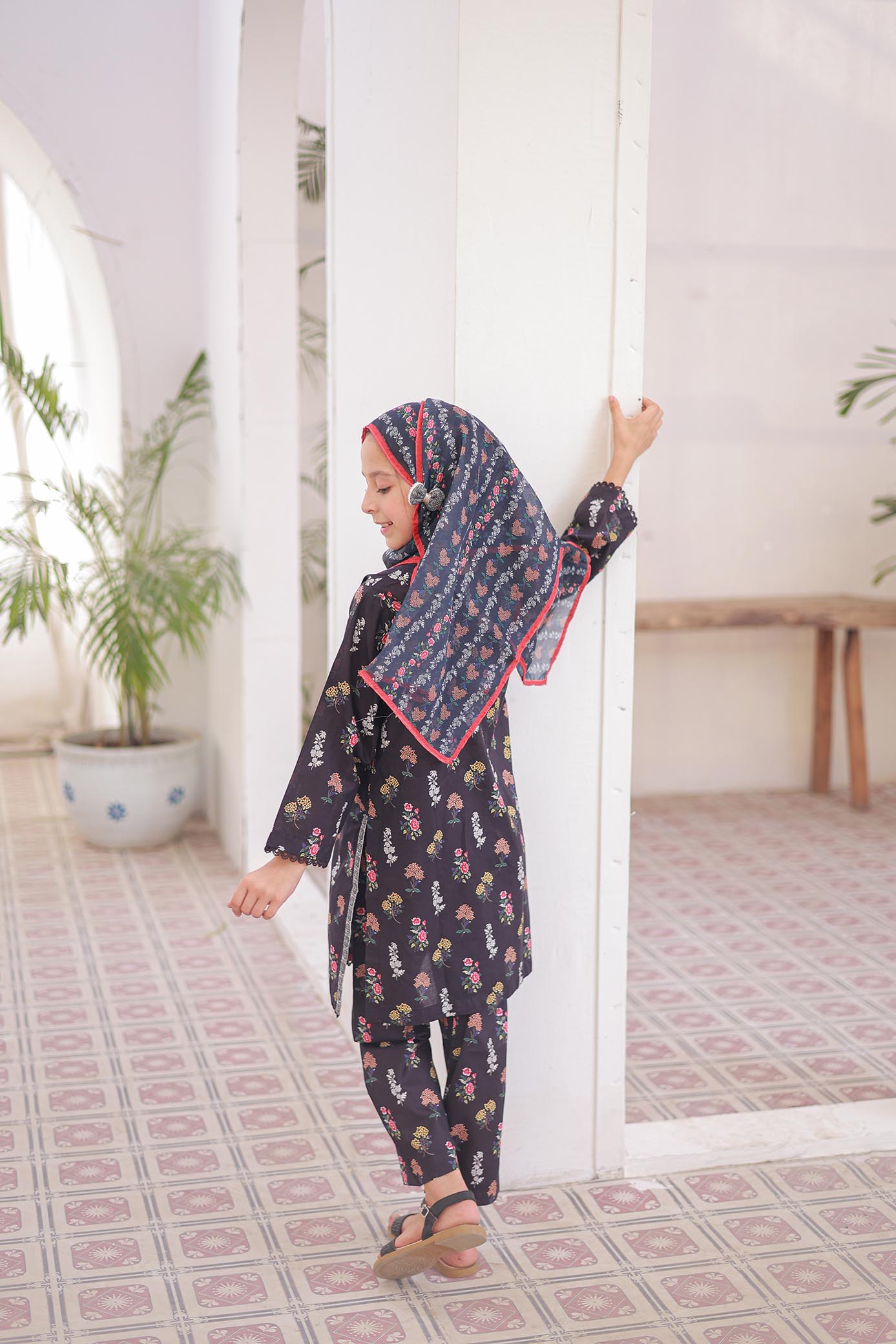 Woman in a patterned outfit standing in a room with plants and a mirror.
