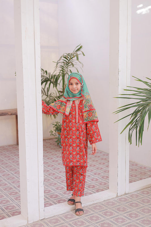 Child wearing a red and green traditional outfit with a headscarf, standing in a room with plants.