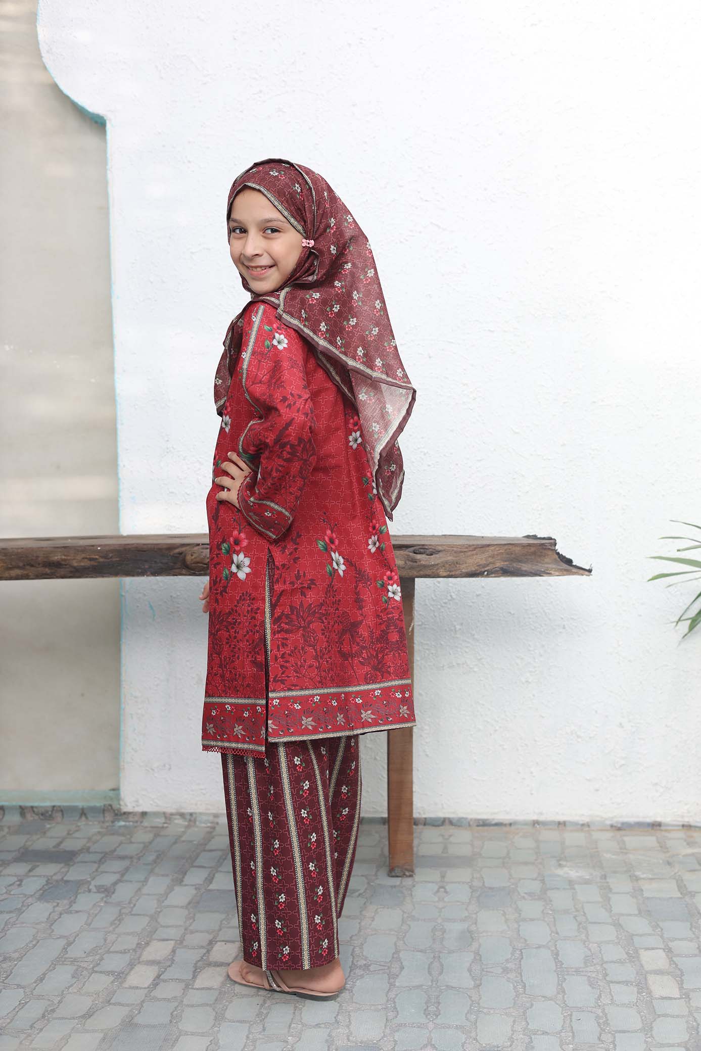 Woman wearing a red traditional outfit with a matching headscarf against a white wall.