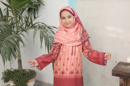 Young girl in a pink and red traditional outfit standing indoors with plants in the background