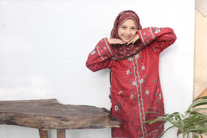 Woman in a red traditional outfit with floral patterns standing indoors.