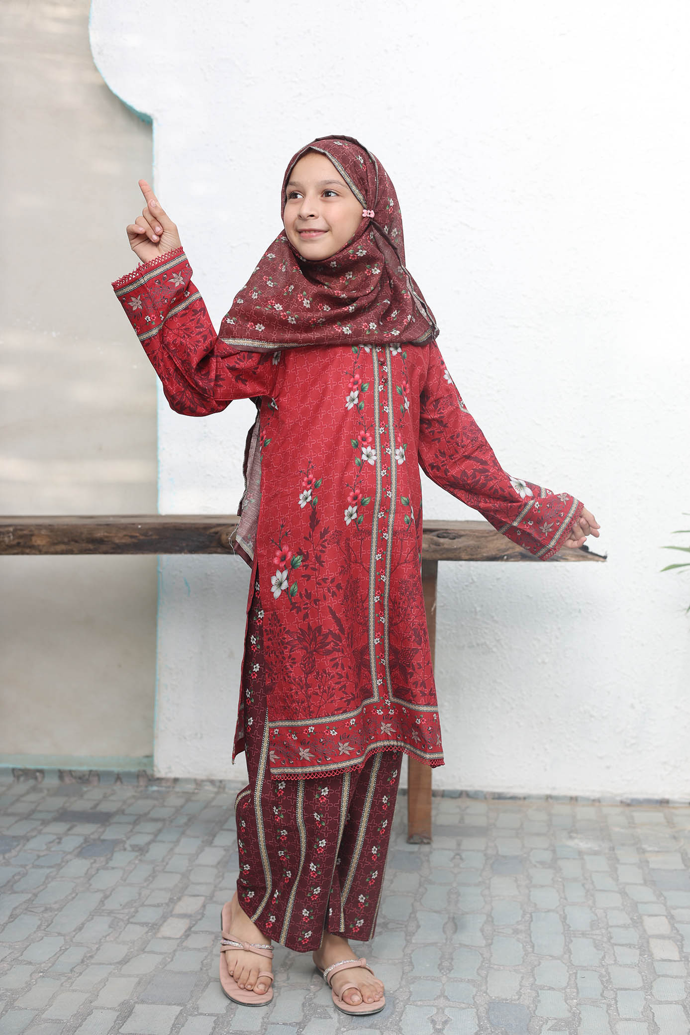 Girl in a red traditional outfit with floral patterns standing on a bench.