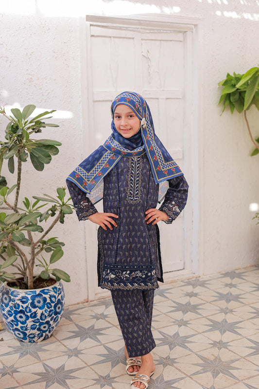 A girl wearing a navy blue, embroidered, long-sleeved shirt with a dupatta, standing against a white background with a potted plant beside her.