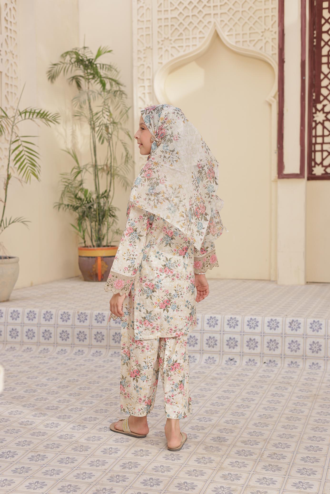 Woman in a floral outfit standing in a room with decorative tiles and plants.