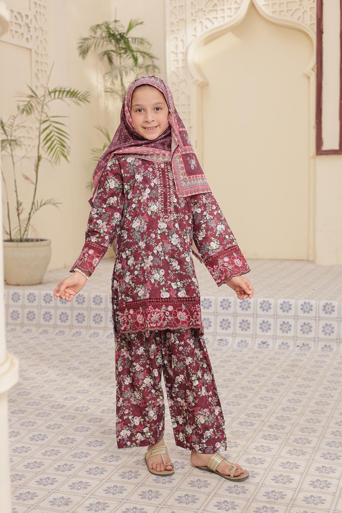Child wearing a floral outfit with a matching headscarf in a decorated room.