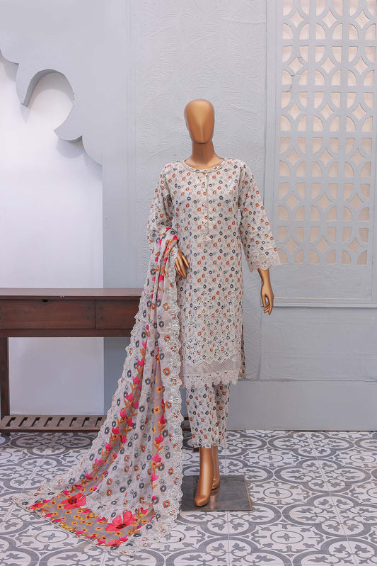 A three-piece beige festive embroidered outfit consisting of a shirt with front and sleeve embroidery, laser and cutwork embellishments, trousers, and a dupatta with printed cutwork, displayed on a mannequin against an indoor backdrop.