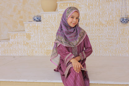 Young girl in a purple traditional outfit sitting on a white step.