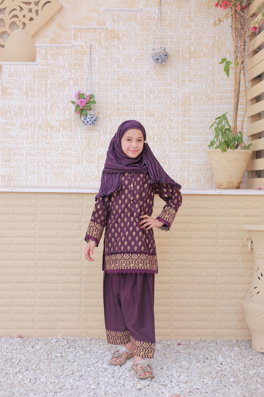 Girl in a purple traditional outfit with a matching hijab standing against a decorative wall.