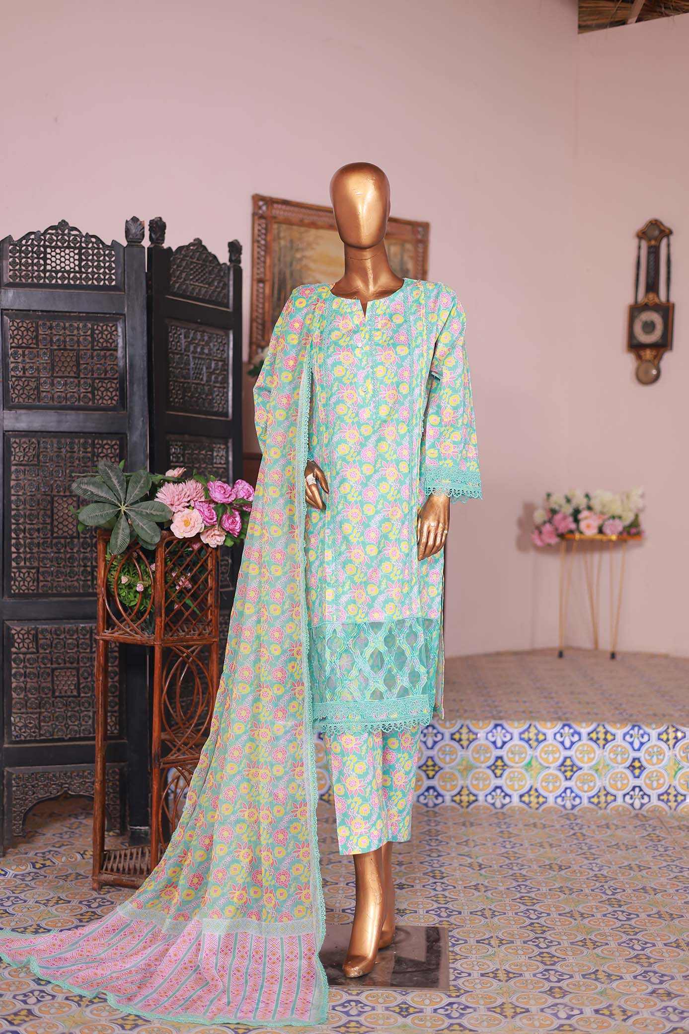 A long-sleeved shirt with turquoise embroidery, paired with a printed cambric trouser and a matching dupatta, displayed on a mannequin against an interior backdrop.