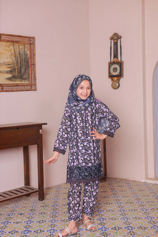 A girl wearing a long-sleeved embroidered shirt with laser lace cutwork, paired with a printed dupatta and trousers, standing in a room with a patterned floor.