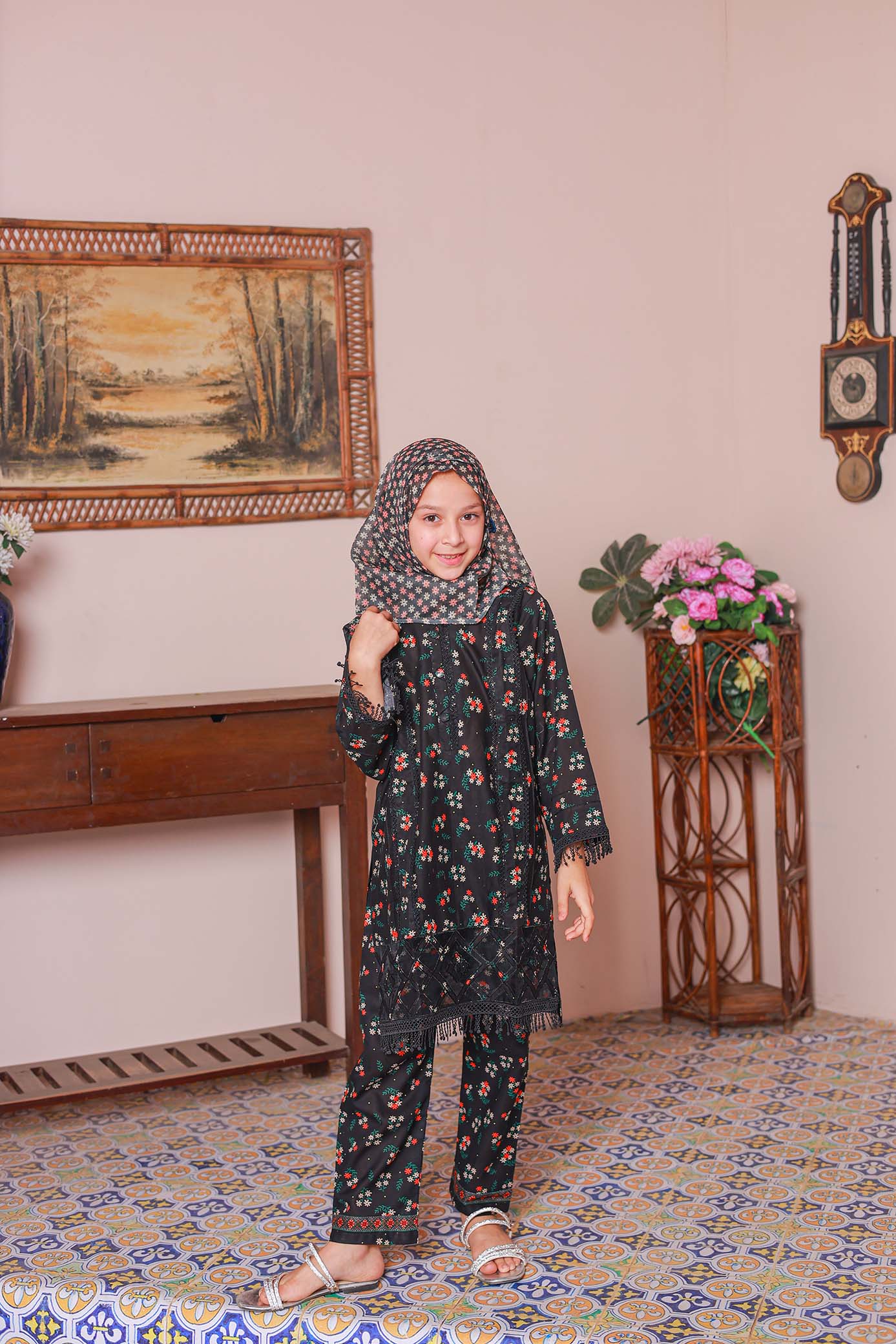 A girl wearing a black embroidered shirt with long sleeves, paired with a printed dupatta and matching trousers, standing in an indoor setting.