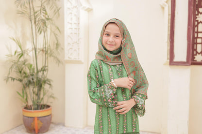 Young girl in a green traditional outfit with a headscarf standing indoors.