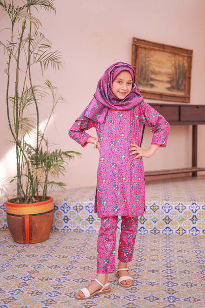 A girl wearing a long-sleeved fuchsia printed shirt with dupatta and matching trousers, standing indoors.