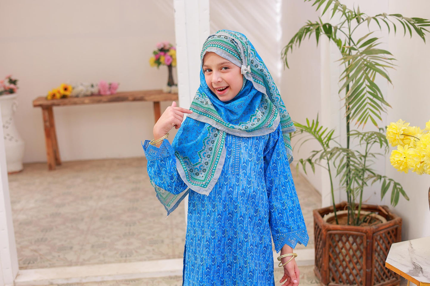 A woman posing in a blue printed shirt with embroidery and lacework, along with matching printed trousers and a dupatta.
