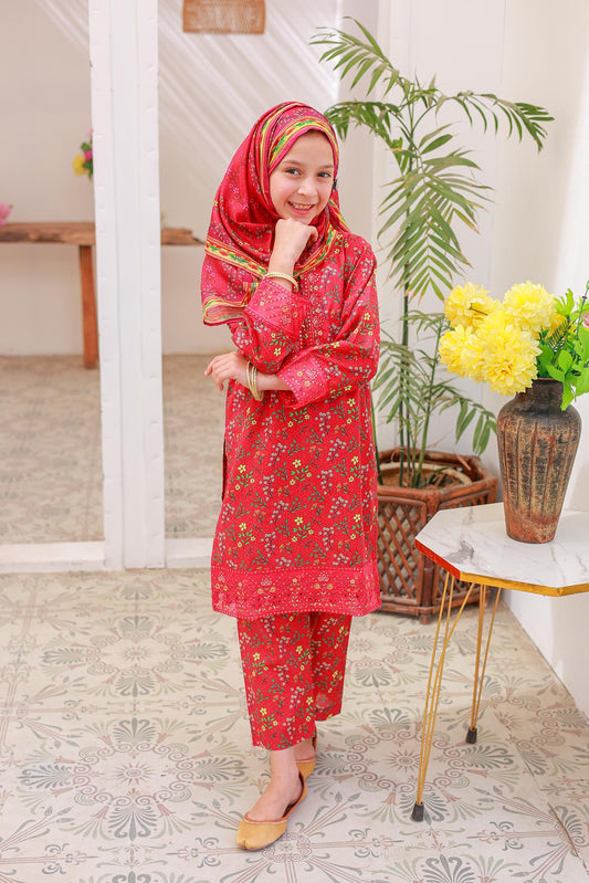 A woman wearing a red floral embroidered shirt with long sleeves, paired with matching trousers and a dupatta, standing in a room with a light-colored background.